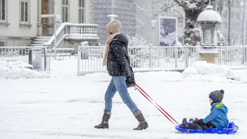 Eine Frau spaziert mit einem Knaben bei Schneegestöber über die Churer Bahnhofstrasse. 