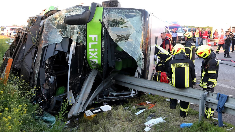 Einsatzkräfte der Feuerwehr stehen an der Unfallstelle neben dem verunglückten Bus in der Nähe von Leipzig.