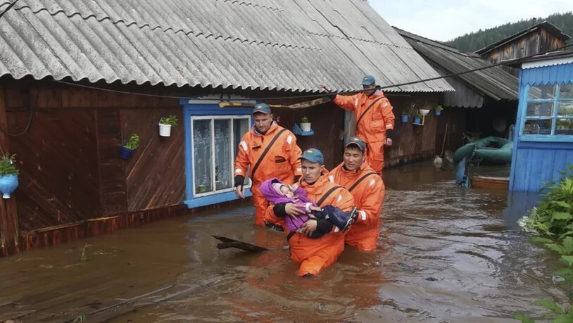 Helfer bringen ein Kind aus einem überfluteten Haus in Sicherheit.