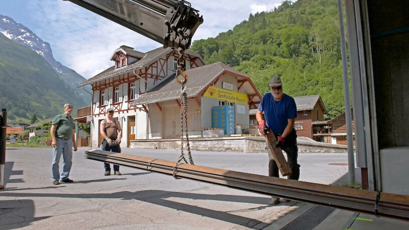 Anlieferung der Schienen in Elm: Vereinsmitglieder packen tatkräftig an, im Hintergrund ist das Stationsgebäude Elm mit angebautem Güterschuppen zu sehen.