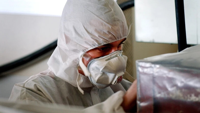 Ein Arbeiter mit Mundschutz und Schutzkleidung bereitet eine Abfallkiste voll asbestverseuchtem Material auf ihren Abtransport vor. (Archivbild)