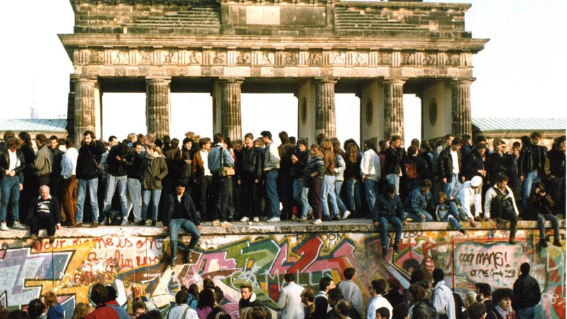 Am Tag nach der Öffnung am 9. Nov. 1989 steigen Menschen am 10. Nov. 1989 auf die Berliner Mauer vor dem Brandenburger Tor in Berlin. (Archivbild)
