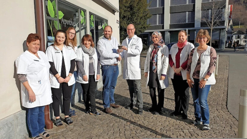 Der Inhaber wechselt, das Personal bleibt: Reto Moor (Mitte, links) überreicht dem neuen Besitzer Oliver Kuonen symbolisch Mörser und Stössel, umringt sind sie von den Mitarbeiterinnen, die weiterhin der der Apotheke Glarus arbeiten werden.