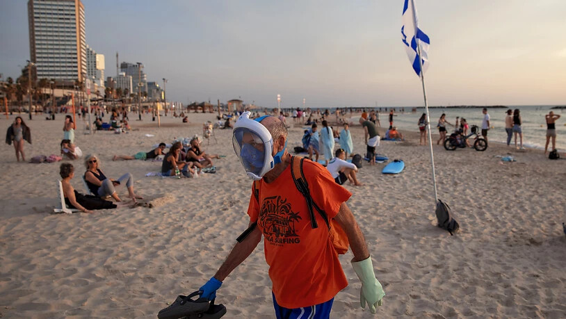 Ein älterer Mann trägt Handschuhe und eine Tauchermaske, die er als schützende Gesichtsmaske an der Strandpromenade verwendet. Foto: Oded Balilty/AP/dpa
