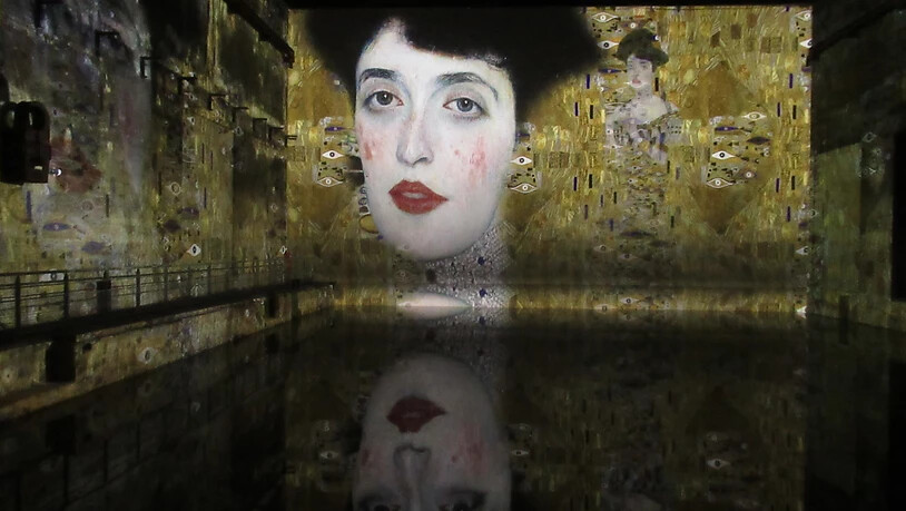 «Die Frau in Gold» von Gustave Klimt spiegelt sich im «Bassins de Lumières». Foto: Sabine Glaubitz/dpa - ACHTUNG: Nur zur redaktionellen Verwendung im Zusammenhang mit einer Berichterstattung über die Ausstellung und nur mit vollständiger Nennung des…
