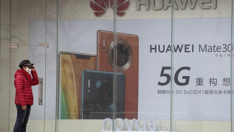 ARCHIV - Eine Frau mit Mundschutz steht vor einer Werbung für Smartphones von Huawei. China hat zwei festgehaltene Kanadier offiziell wegen Spionagevorwürfen angeklagt. Foto: Ng Han Guan/AP/dpa