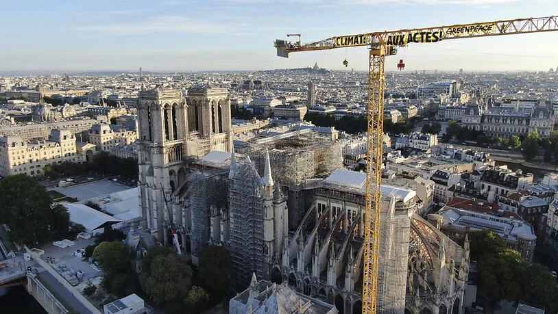 HANDOUT - Ein Transparent: "Klima. In Aktion" ist an einem Kran an der Baustelle der Kathedrale Notre Dame befestigt. Mit einer Aktion auf der Baustelle der Kathedrale Notre-Dame hat die Umweltschutzorganisation Greenpeace in Paris für Aufsehen gesorgt…
