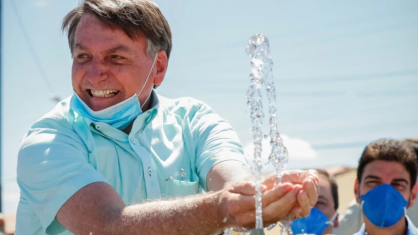 HANDOUT - Auf diesem vom brasilianischen Präsidentenamt zur Verfügung gestellten Bild lächelt Jair Bolsonaro, Präsident von Brasilien, mit untergezogenem Mundschutz, während er an einem Brunnen zur lokalen Wasserversorgung mit Wasser spielt. Foto: Alan…