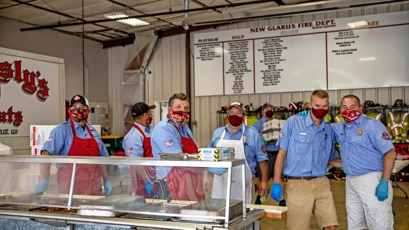 Die fleissigen Köche von New Glarus: Um Geld für die Feuerwehr zu generieren, veranstaltet das New Glarus Fire Department ein Kalberwurst-Essen. Spass macht das offensichtlich auch mit Maske. 