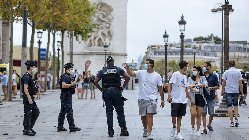 dpatopbilder - Touristen mit Schutzmasken gehen auf der Prachtstraße Champs-Elysees an Polizisten vorbei. Foto: Kamil Zihnioglu/AP/dpa