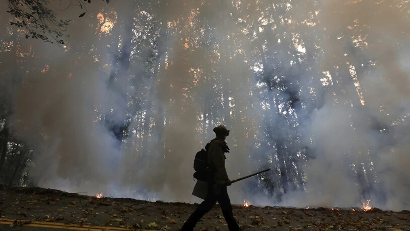 Ein Feuerwehrmann geht am Rande eines Gegenfeuers, welches die Brände in einem Waldgebiet unter Kontrolle bringen soll. Foto: Shmuel Thler/The Santa Cruz Sentinel/dpa