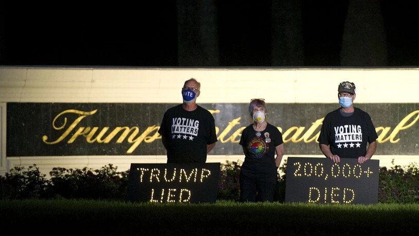 Die Demonstranten Mark Beaumont (l-r), Joyce Brown und Bruce Brown halten in der Nähe des Trump International Golf Club eine Mahnwache ab. In den USA sind inzwischen über 200 000 Menschen nach einer Corona-Infektion gestorben. Foto: Meghan Mccarthy/Palm…