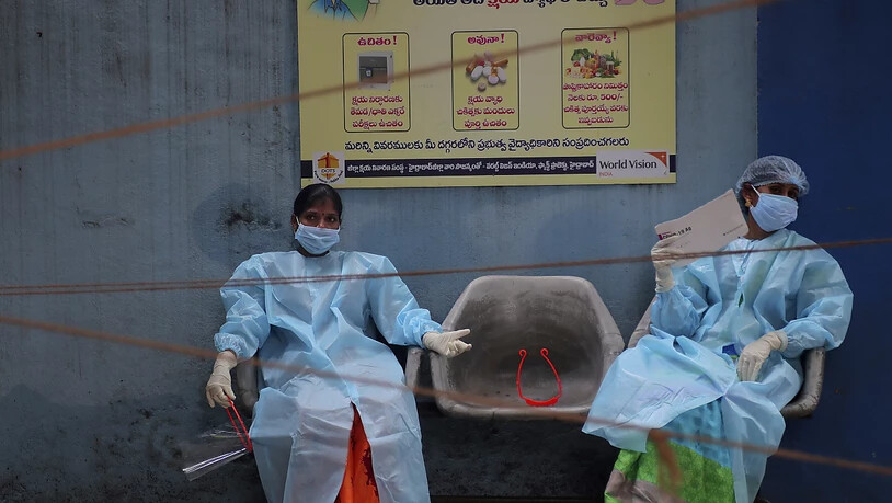 Medizinische Mitarbeiterinnen in Schutzausrüstung ruhen sich vor der Entnahme von Speichelproben für Covid-19-Tests aus. Foto: Mahesh Kumar A/AP/dpa