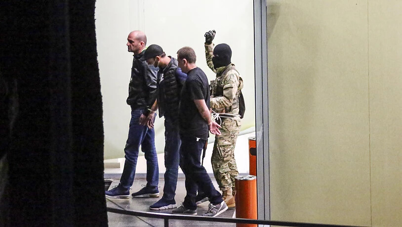 dpatopbilder - Ein Geiselnehmer (r) mit einer Waffe und einer Handgranate in der Hand läuft hinter drei mit Kabelbindern gefesselten Polizisten, die er als Geiseln genommen hat, aus einem Bankgebäude in Westgeorgien. Der bewaffnete Mann forderte eine…