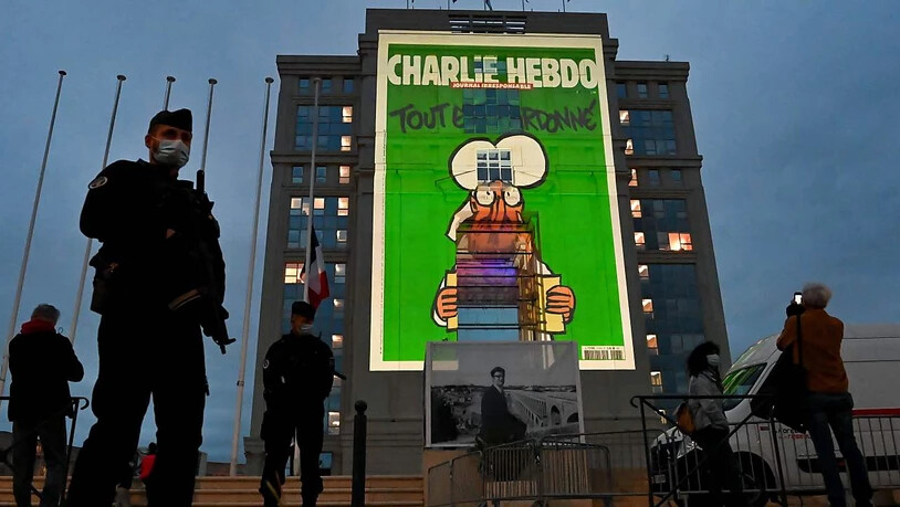 Polizeibeamte stehen Wache, während bei einer landesweiten Gedenkveranstaltung an den ermordeten Lehrer Samuel Paty Karikaturen der französischen Satirezeitung Charlie Hebdo auf die Fassade des Hotel de Region in Montpellier projiziert werden. Foto:…