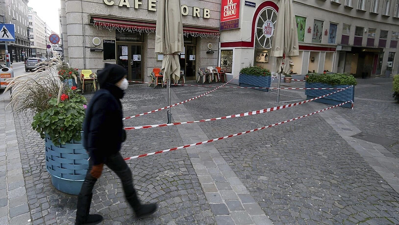 Ein Mann mit Mund-Nasen-Schutz geht an einem geschlossenen Cafe in der Wiener Innenstadt vorbei. Foto: Ronald Zak/AP/dpa