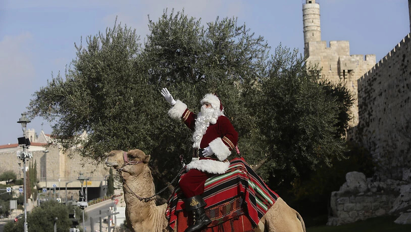 Ein Mann in einem Weihnachtsmann-Kostüm sitzt auf einem Kamel außerhalb der Altstadt von Jerusalem. Foto: Mahmoud Illean/AP/dpa