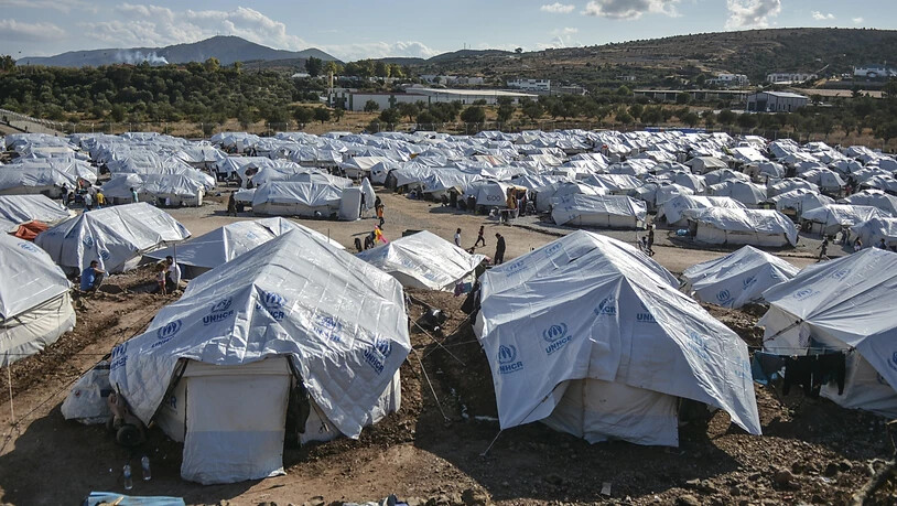 ARCHIV - Migranten gehen nach starken Regenfällen durch das Flüchtlingslager «Kara Tepe». Das provisorische Zeltlager «Kara Tepe» war in Windeseile errichtet worden, nachdem das ursprüngliche Lager Moria bei einem Großbrand fast völlig zerstört worden…