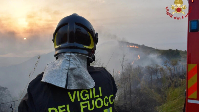 HANDOUT - Ein Feuerwehrmann steht vor einem Gebiet, in dem mehrere Brände lodern (Aufnahmeort unbekannt). Weit über 1000 Einsätze leistete die italienische Feuerwehr in den letzten 24 Stunden, um zahlreiche Waldbrände auf dem süditalienischen Festland…