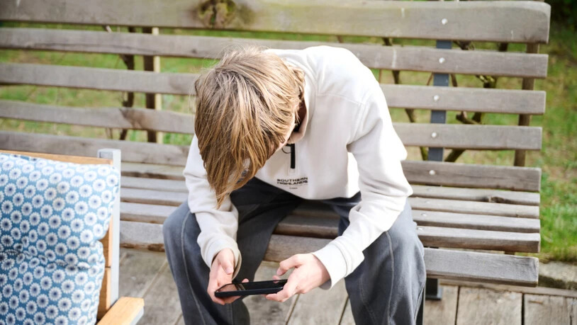 ILLUSTRATION - Ein Jugendlicher sitzt auf einer Bank und schaut auf sein Smartphone. Australien hat ein Social-Media-Verbot für Kinder und Jugendliche unter 16 Jahren eingeführt und ist damit weltweiter Vorreiter. (zu dpa: «Australien: Social-Media…