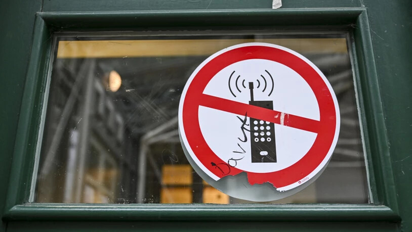 ARCHIV - Ein Schild mit einem durchgestrichenen Handysymbol weist in einer Schule auf das Handyverbot hin. Foto: Jens Kalaene/dpa/Symbolbild
