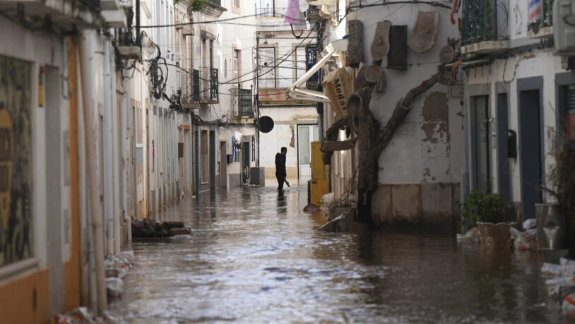 Ein Anwohner geht eine überflutete Straße entlang, nachdem der Fluss Sado nach heftigen Regenfällen in Alcácer do Sal, Südportugal, über die Ufer getreten ist. Foto: Ana Brigida/AP/dpa