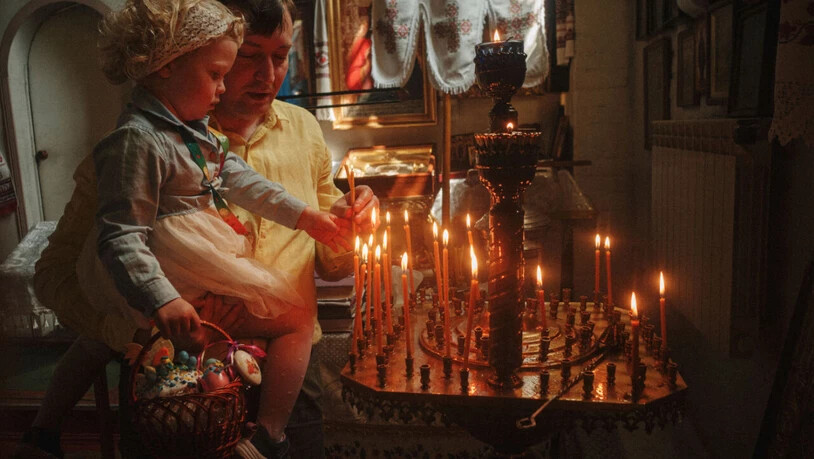 Ein Vater hilft seiner Tochter beim Anzünden einer Kerze während der orthodoxen Osterfeier in der St. Johannes Theologen Kirche der Orthodoxen Kirche der Ukraine in Charkiw. Am Wochenende sollen es in der Ukraine eine Waffenruhe geben, damit die Menschen…