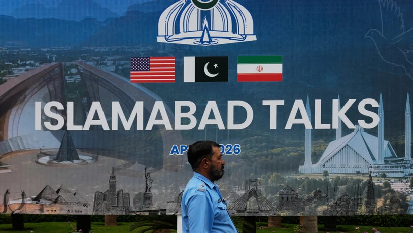 Ein Polizeibeamter geht vor einem Medienzentrum an einer Plakatwand zu den Verhandlungen zwischen den USA und dem Iran vorbei. Foto: Anjum Naveed/AP/dpa