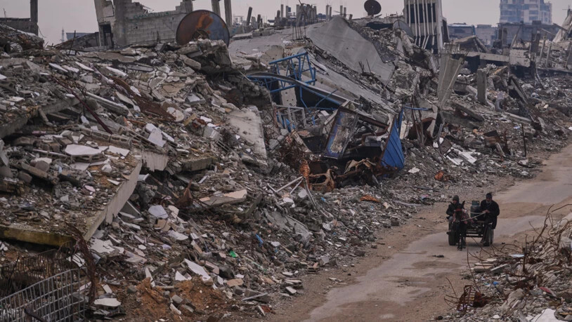 ARCHIV - Palästinenser gehen eine Straße in der Stadt Gaza entlang, die von Gebäuden umgeben ist, die bei israelischen Luft- und Bodenangriffen im Viertel Sheikh Radwan zerstört wurden. Foto: Abdel Kareem Hana/AP/dpa