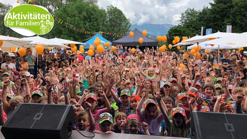 Die Hände hoch zum Himmel: Fröhliche Kinder posieren am Kinderland Open Air in Arosa für ein Gruppenbild.