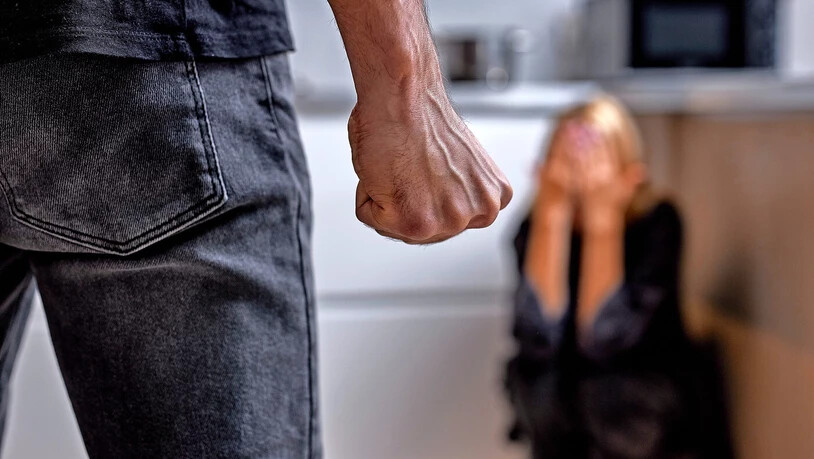 Mit geballter Faust: Ein Mann baut sich vor seiner Partnerin auf, die in der Küchenecke hockt.