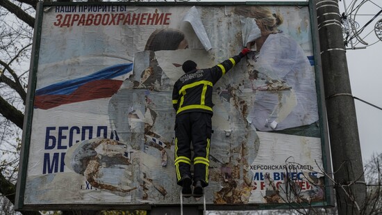 Ein ukrainischer Feuerwehrmann reißt in der kürzlich befreiten Stadt Cherson eine russisches Werbeplakat von einer Werbetafel. Foto: Bernat Armangue/AP/dpa