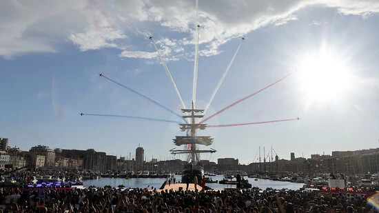 Das olympische Feuer kommt, begleitet von einer Flug-Show, per Schiff im Hafen von Marseille an