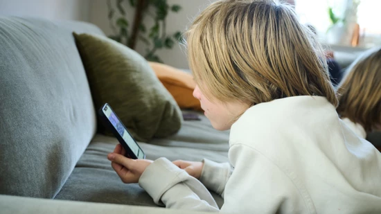 ARCHIV - ILLUSTRATION - Ein Junge liegt auf einem Sofa und guckt auf sein Smartphone. (gestellte Szene). Australien hat ein Social-Media-Verbot für Kinder und Jugendliche unter 16 Jahren eingeführt und ist damit weltweiter Vorreiter. Foto: Annette Riedl…