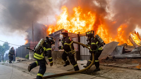 Feuerwehrleute bekämpfen ein Feuer in einem Haus, während Waldbrände lodern. Foto: Javier Torres/AP/dpa