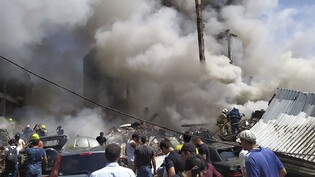 Zivilisten und Feuerwehrleute befinden sich an der Unfallstelle während Rauch aufsteigt. Nach einer schweren Explosion in einem Einkaufszentrum sind nach offiziellen Angaben einige Menschen verletzt oder tot. Foto: Daniel Bolshakov/AP/dpa