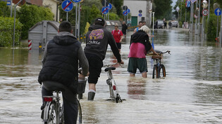 Ein Mann fährt auf einem Fahrrad eine überflutete Straße in Barbiano di Cotignola entlang. Foto: Luca Bruno/AP/dpa