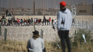 Migranten stellen sich an der US-Grenzmauer auf, nachdem sie von den US-Einwanderungsbehörden festgehalten wurden. Bewaffnete haben im Nordosten von Mexiko an der Grenze zu den USA 31 Migranten aus einem Bus entführt. Foto: Christian Chavez/AP
