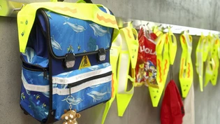 Schulrucksäcke und Leuchtgurte am ersten Schultag vor einem Schulzimmer.