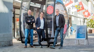 Ausstellungsstück: Die Projektverantwortlichen der Churer Bergbahnen Patrick Arnet, Nina Vuillemin und Reto Küng (von links) posieren um die bis zum 1. Oktober ausgestellte Gondel in der Churer Poststrasse.